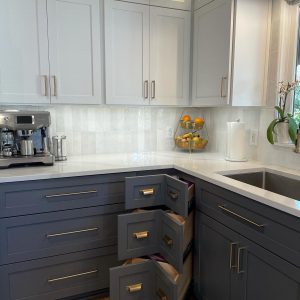 A beautiful kitchen with new-looking cabinets, white countertops, and navy drawers that are slightly opened