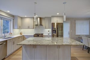 A modern kitchen with an large central island that is topped with a stone countertop