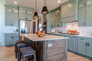 A beautiful kitchen with an isaldn as well as stainless steel appliances and light teal cabinets